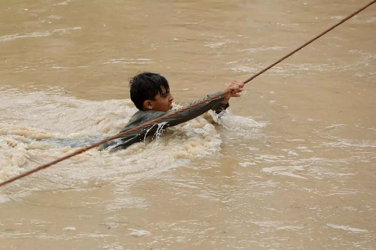A boy crosses a flooded street, with the help of a wire fastened on both ends, following rains and floods during the monsoon season in Charsadda, Pakistan 