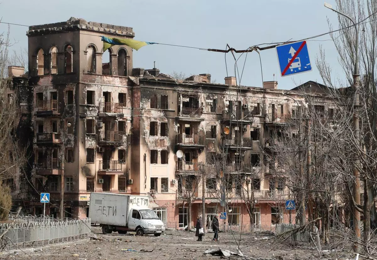 Local residents walk along a street next to a building damaged during Ukraine-Russia conflict in the southern port city of Mariupol, Ukraine April 3, 2022. The sign on the vehicle reads: “Children”. 