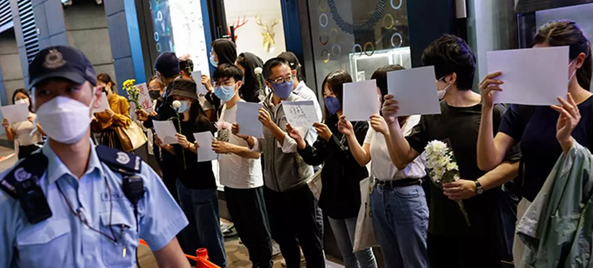 People hold white sheets of paper and flowers in a row as police check their IDs during a protest over coronavirus disease (COVID-19) restrictions in mainland China, during a commemoration of the victims of a fire in Urumqi, in Hong Kong, China.