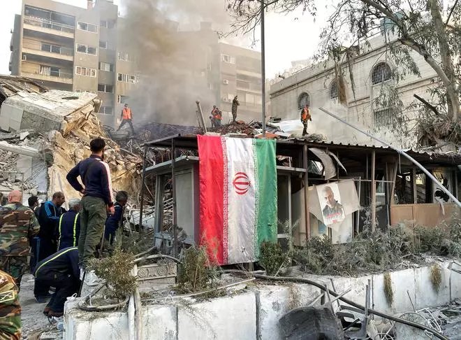 An Iranian flag hangs as smoke rises after what the Iranian media said was an Israeli strike on a building close to the Iranian embassy in Damascus, Syria April 1, 2024. 