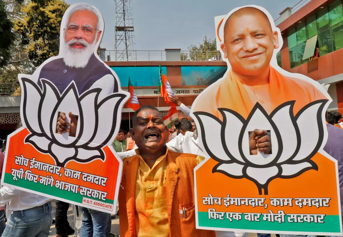 A BJP supporter displays cut-outs of Prime Minister Narendra Modi and Uttar Pradesh Chief Minister Yogi Adityanath as he celebrates after learning the initial poll results outside its party office in Lucknow on Thursday