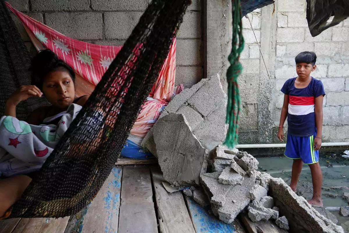 A woman holding her baby looks at the destroyed wall of her house following an earthquake in Isla Puna, Ecuador on Saturday.