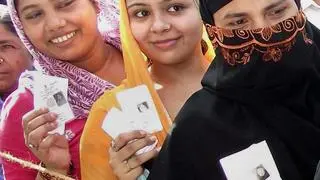 Women voters show their voter ID cards as they stand in queue at a polling station. Women voters show their voter ID cards as they stand in queue at a polling station.