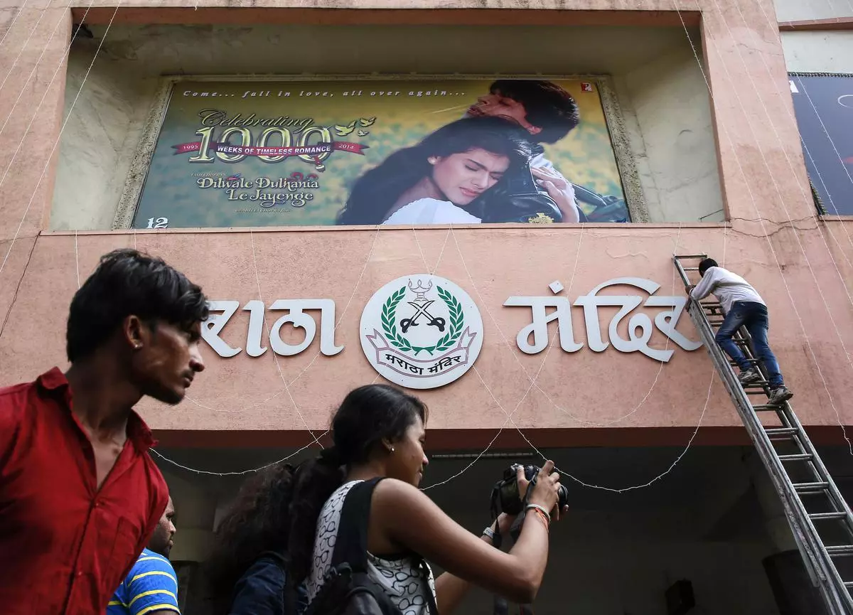 File Photo: A cinemagoer takes pictures as an employee prepares a hoarding of Bollywood movie “Dilwale Dulhania Le Jayenge” (The Big Hearted Will Take the Bride), starring actor Shah Rukh Khan.