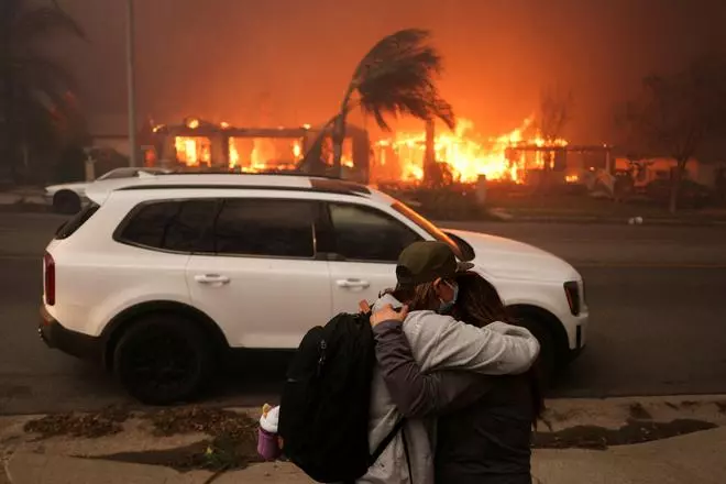 People embrace as they evacuate following powerful winds fueling devastating wildfires in the Los Angeles area, at the Eaton Fire in Altadena, California, U.S. January 8, 2025. 