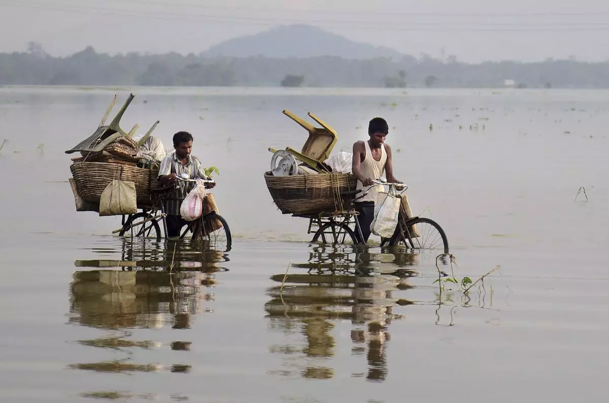 Commuters wade through a flooded area in Kamrup district, June 21, 2022. (PTI)