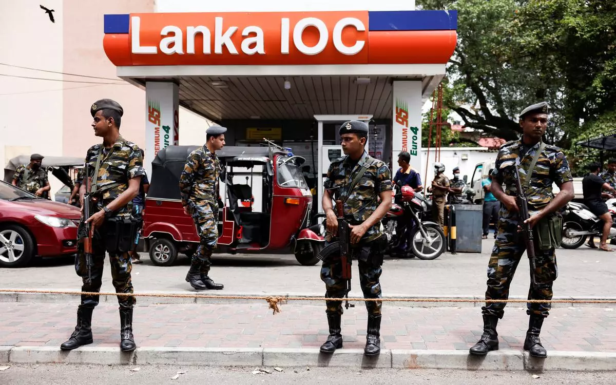 Air Force members stand guard at a Lanka IOC fuel station as people queue up to buy fuel due to fuel shortage