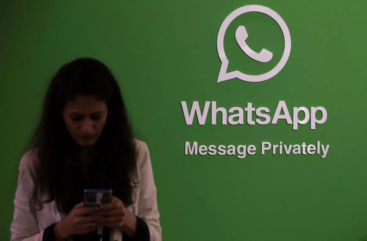 A woman uses her phone next to a logo of the WhatsApp