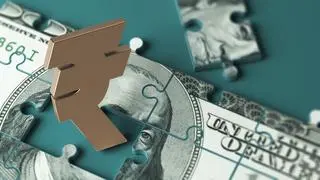 Puzzle-shaped 100 American dollar banknote and gold-colored Indian Rupee symbol. On a charcoal green-colored background. Horizontal composition with copy space. Isolated with clipping path.