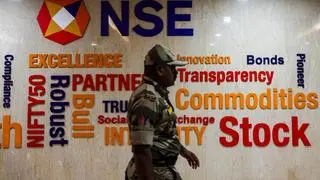 A guard walks past the logo of the National Stock Exchange (NSE) at its headquarters in Mumbai, India