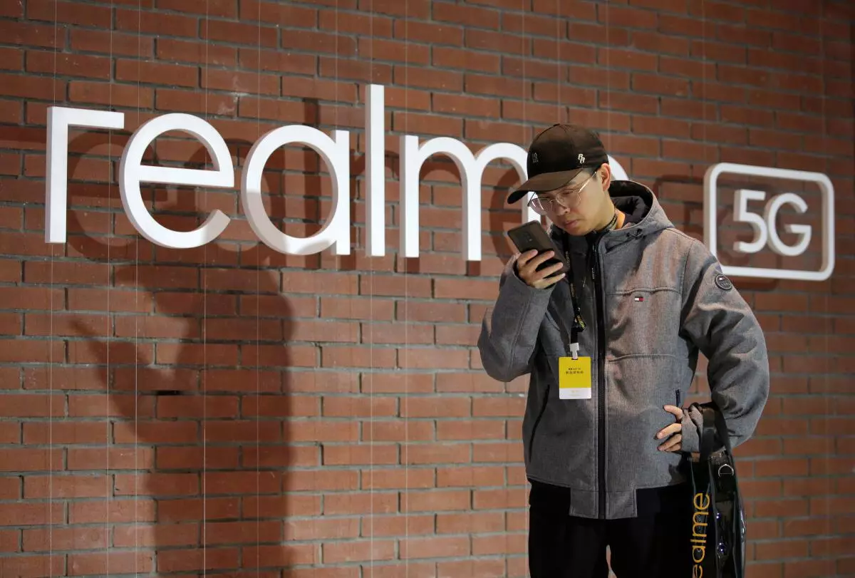 FILE PHOTO: A man looks at his mobile phone next to a logo of Realme during its X50 5G product launch event in Beijing, China January 7, 2020. 