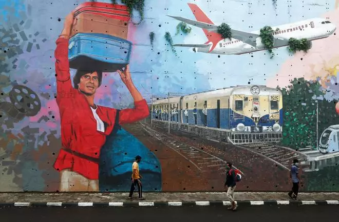 People wearing protective masks walk past a mural of Bollywood actor Amitabh Bachchan.  Reuters