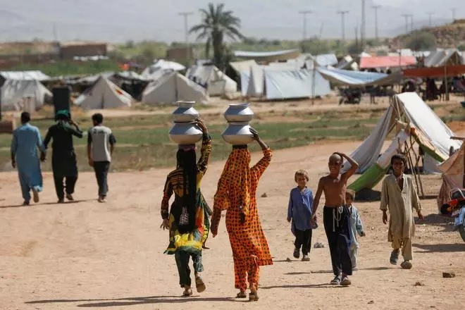 Displaced women walk to their tents in a camp with water pots on their head , following rains and floods during the monsoon season in Sehwan, Pakistan, September 16, 2022. REUTERS