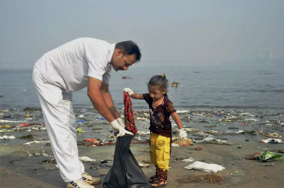 A coastal guard along with a kid participate in a cleaning operation in Mumbai (PTI)